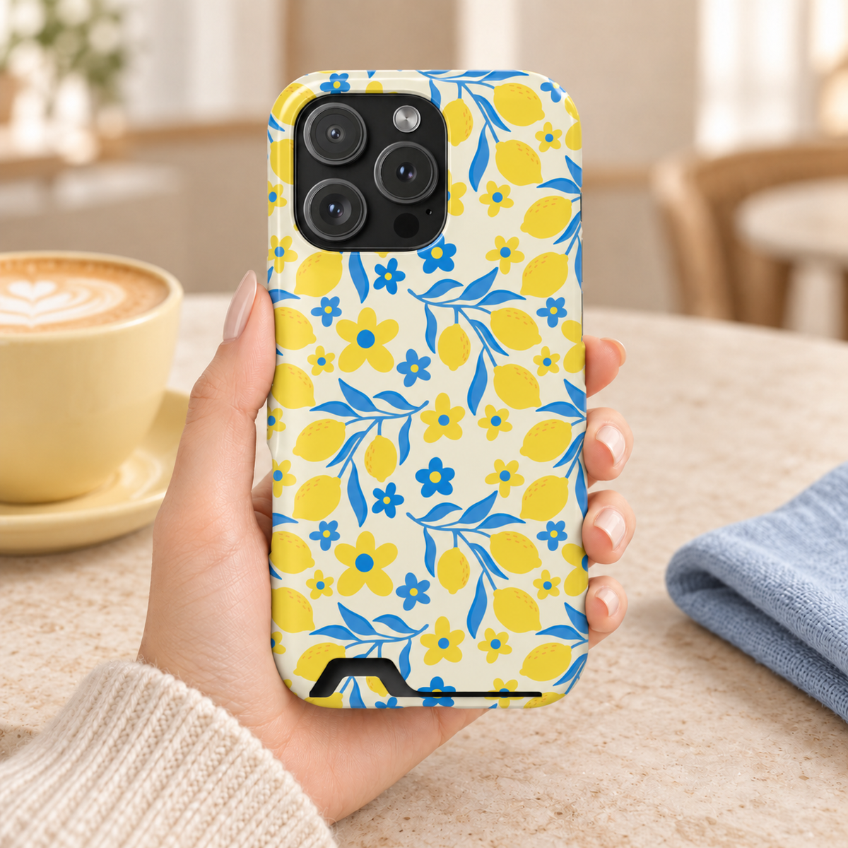 Amalfi Lemon phone case with card holder, yellow lemons and blue leaves on white, lifestyle photo in hand with coffee