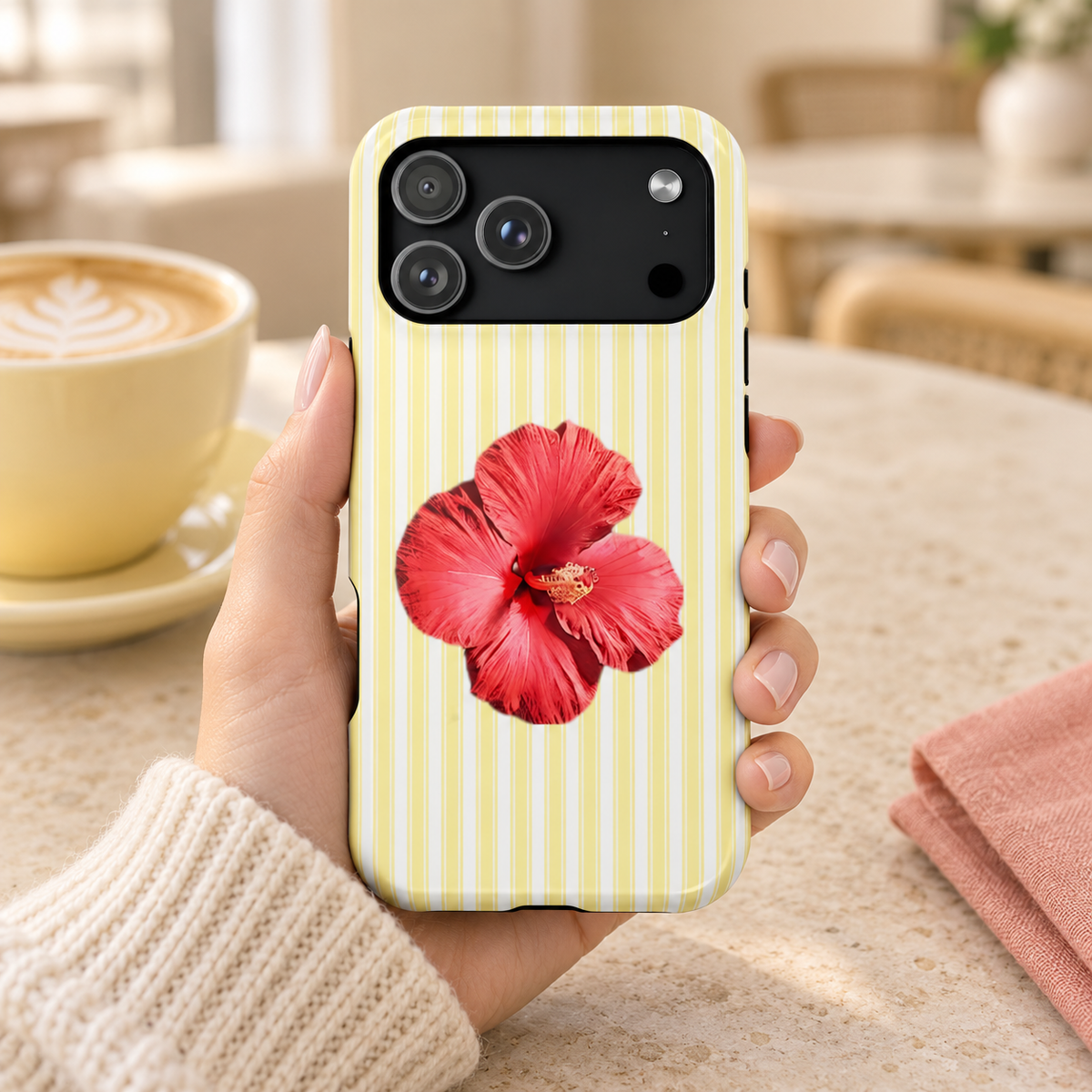 Hibiscus Stripe protective phone case, a red hibiscus on pale yellow stripes, lifestyle photo in hand with coffee