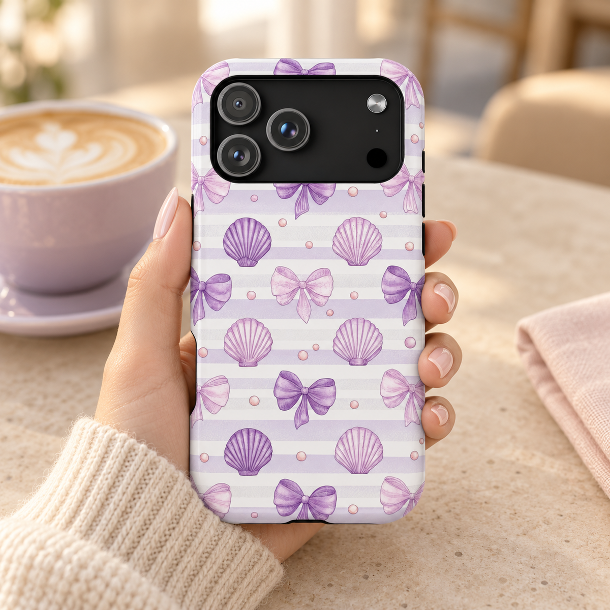 Lilac Seashell MagSafe case, lilac seashells and bows on soft stripes, lifestyle photo in hand with coffee