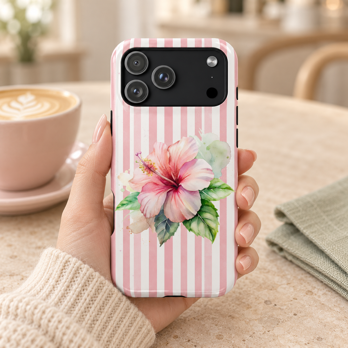 Pink Hibiscus protective phone case, a pink hibiscus on blush stripes, lifestyle photo in hand with coffee