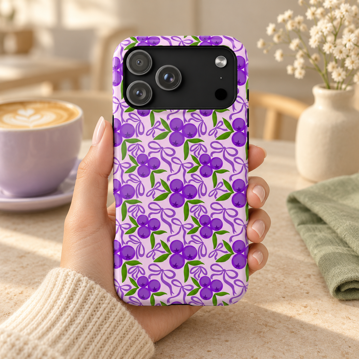 Purple Cherry Bow protective phone case, purple cherries and ribbons on lilac, lifestyle photo in hand with coffee