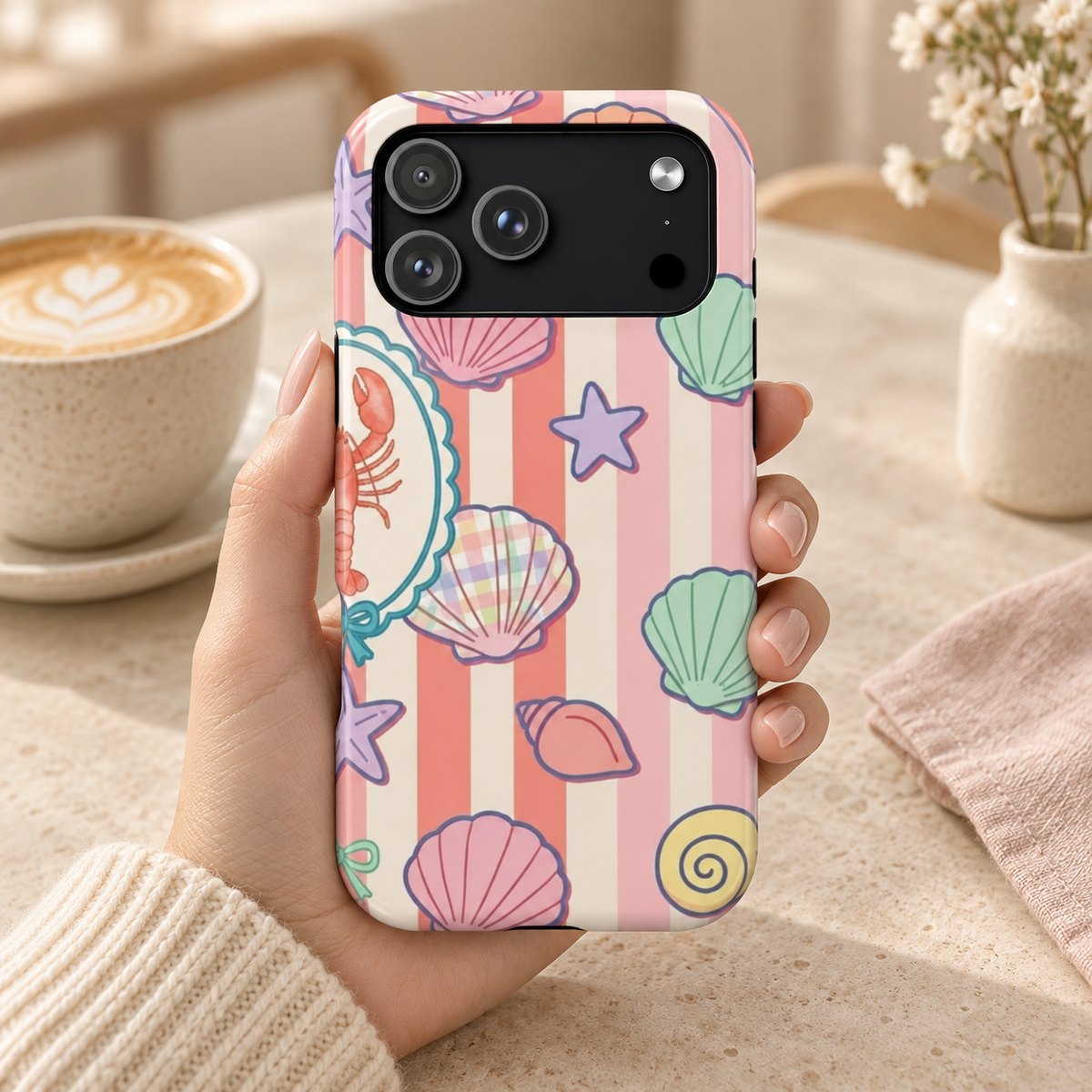 Seashell Stripe MagSafe case, seashells and starfish on coral stripes, lifestyle photo in hand with coffee